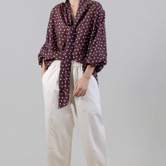 Woman wearing a polka dot shirt and white pants on a gray background