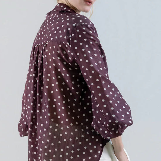 Woman wearing a polka dot blouse and white pants against a plain background