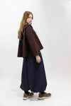 A model is shown from the back wearing a dark brown cape-style jacket, a long navy blue skirt, and brown sneakers against a plain white studio background.
