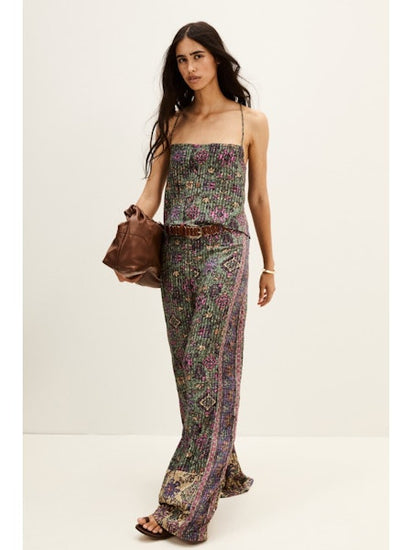 Woman wearing a aztec print top and trousers holding a brown leather bag on a white background