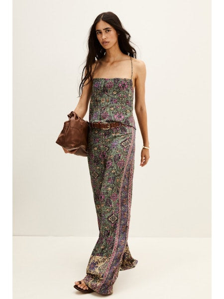 Woman wearing a aztec print top and trousers holding a brown leather bag on a white background