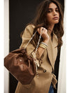 Woman holding a brown leather handbag with a chain strap, wearing a beige blazer.