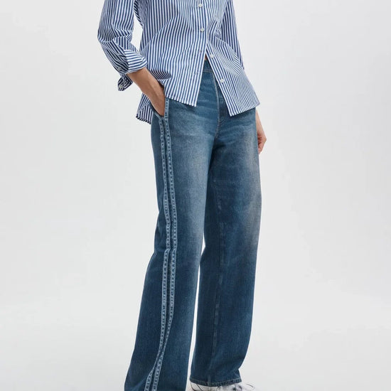 Person wearing a blue and white striped shirt with wide-leg jeans on a white background