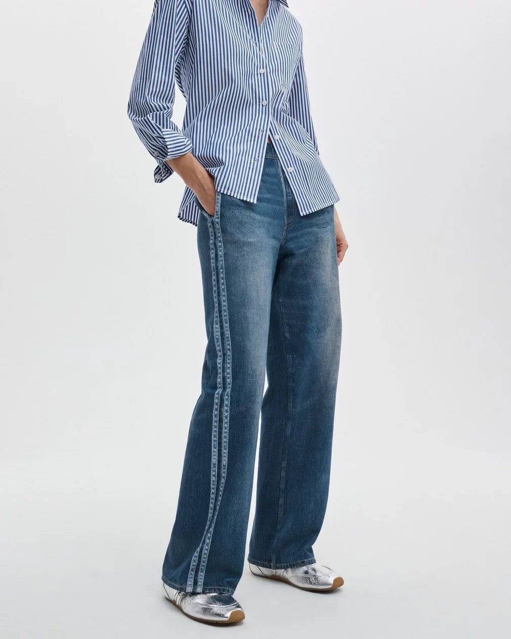 Person wearing a blue and white striped shirt with wide-leg jeans on a white background