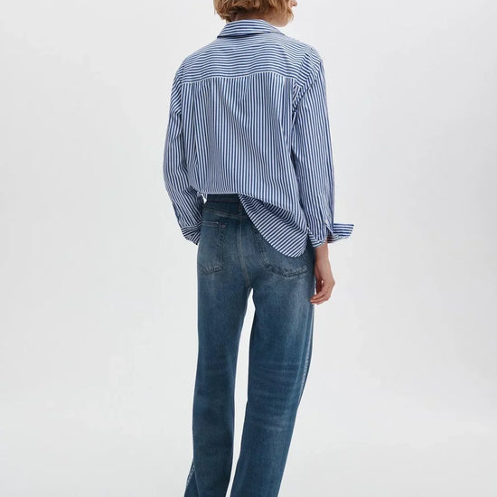 Person wearing a blue and white striped shirt and blue jeans on a white background