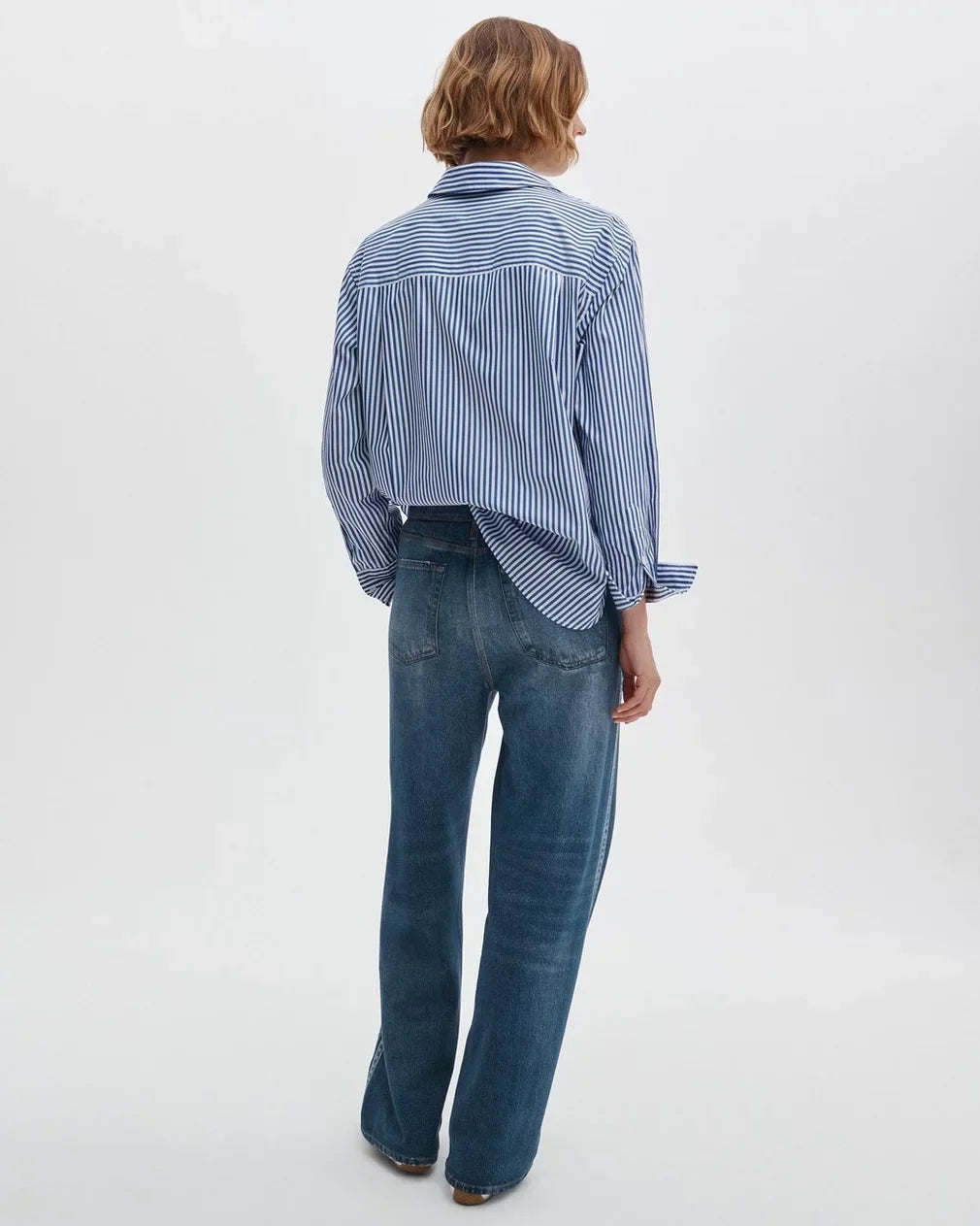 Person wearing a blue and white striped shirt and blue jeans on a white background