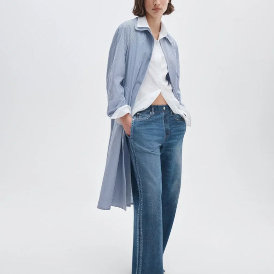 Woman wearing a light blue shirt, white blouse, and blue jeans on a white background