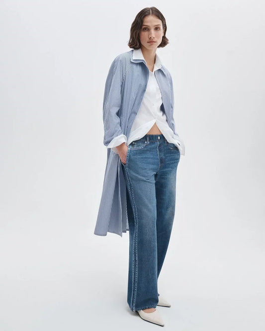 Woman wearing a light blue shirt, white blouse, and blue jeans on a white background