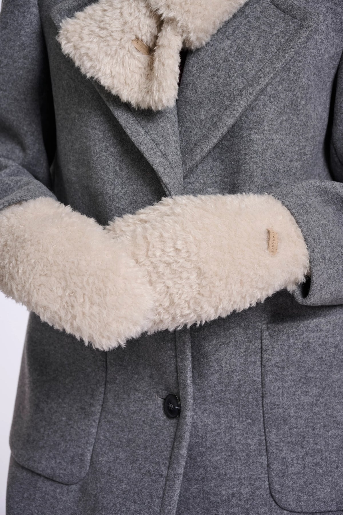 Close-up of a gray wool coat with a thick cream-colored shearling lining on the collar and cuffs, featuring a single black button closure.