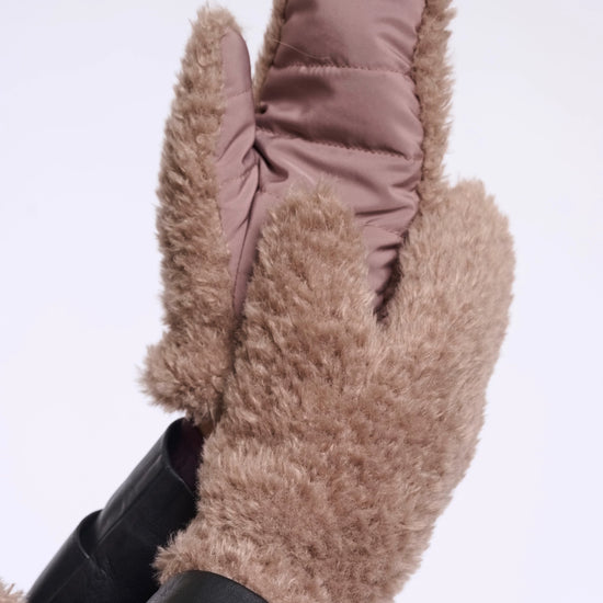 A pair of tan faux-shearling mittens with a smooth taupe quilted lining, shown on a white background with black leather cuffs visible.