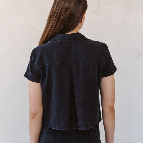 woman wearing black denim short sleeve shirt with white background rear view