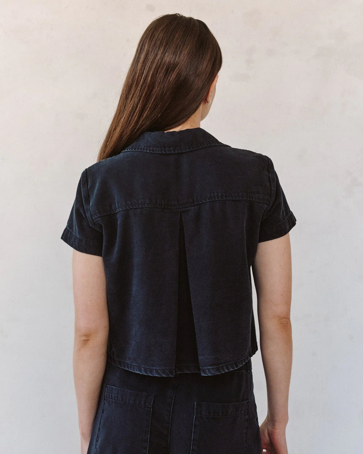 woman wearing black denim short sleeve shirt with white background rear view