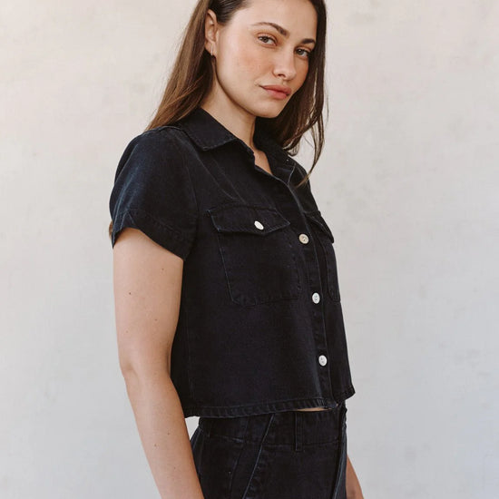 woman wearing black denim short sleeve shirt with white background side view