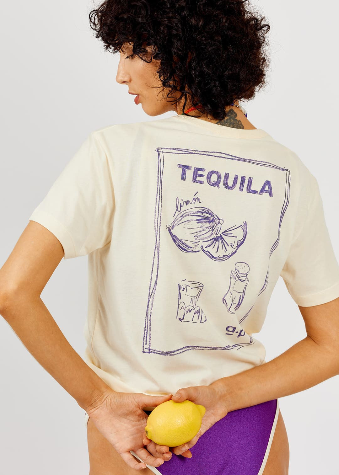 Person wearing a t-shirt with 'Tequila' and lemon graphic, holding a lemon.