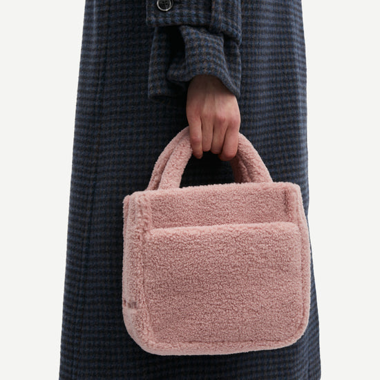 Model holding small faux fur pink bag