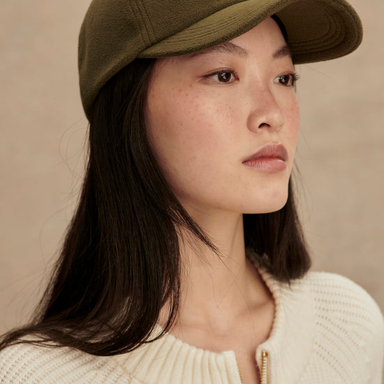 Woman wearing a green cap with a logo on a beige background from Varley