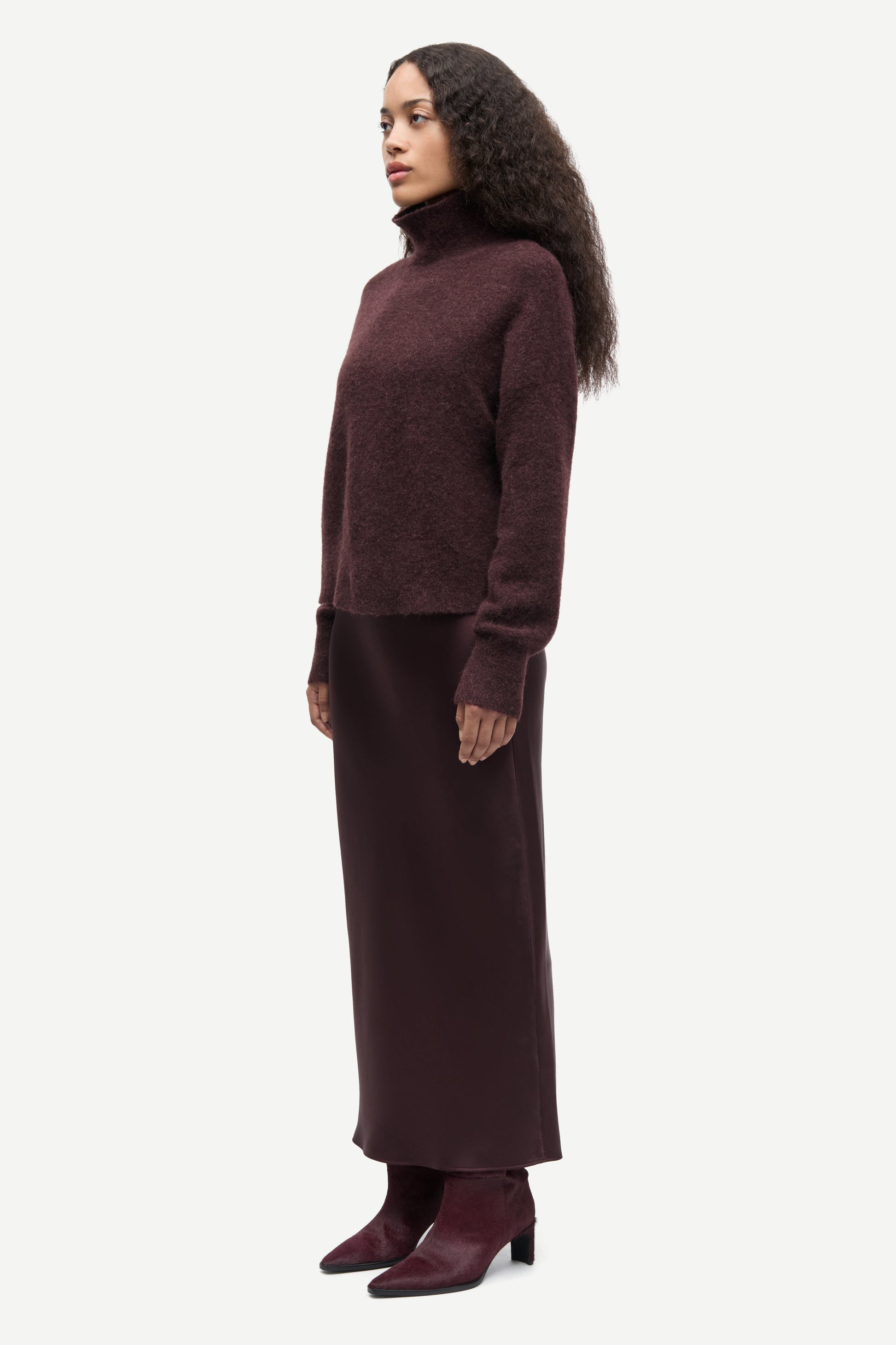 Woman wearing a long burgundy sweater and skirt set on a white background from Samsoe Samsoe