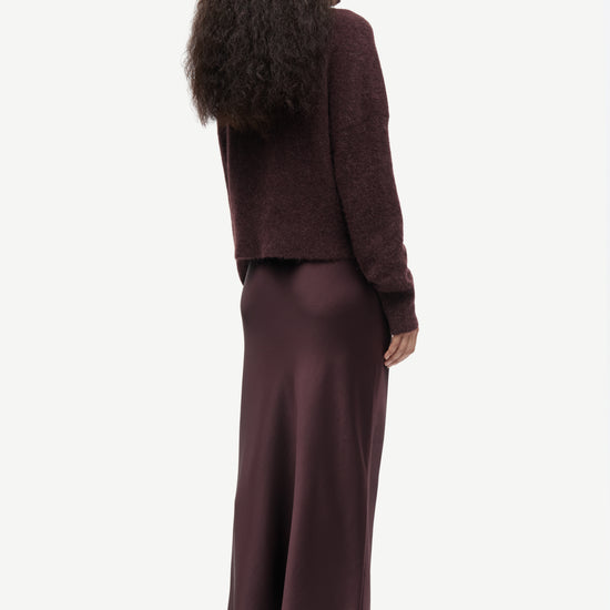 Woman wearing a burgundy brown outfit with a long skirt on a white background