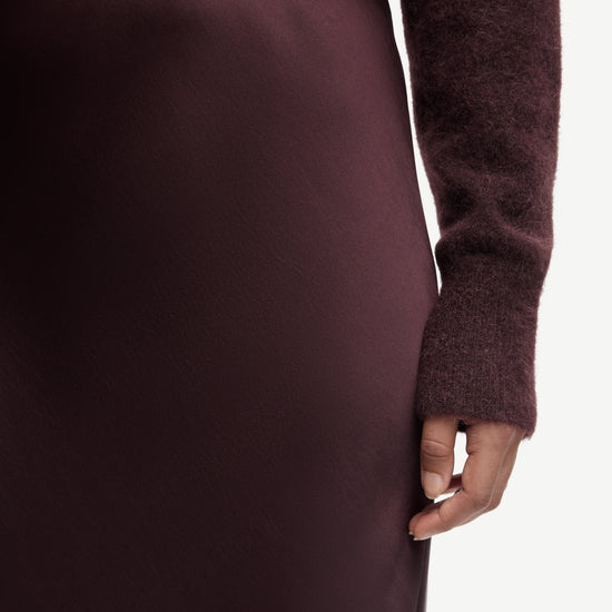 Close-up of a person wearing a burgundy sweater and skirt on a white background