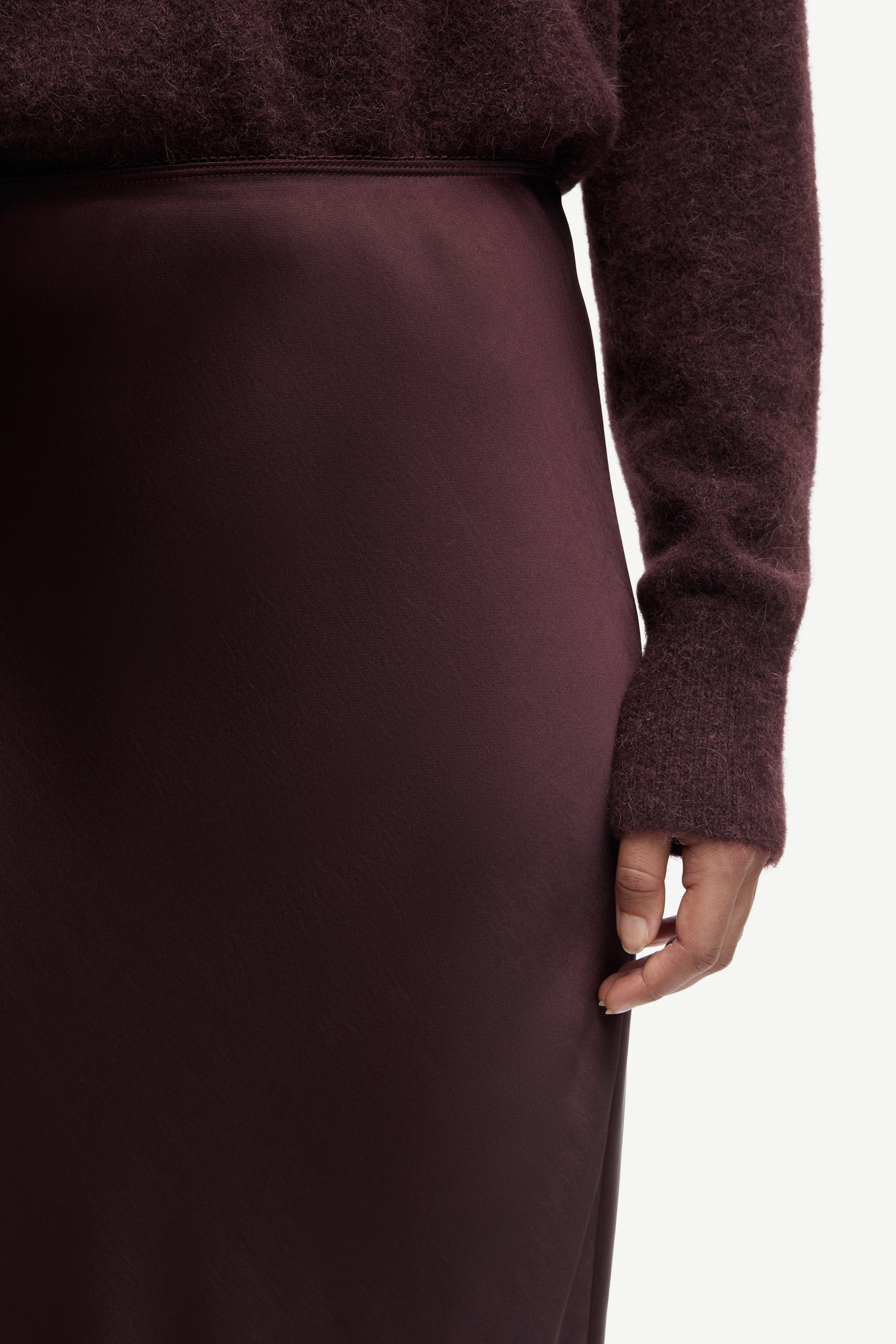 Close-up of a person wearing a burgundy sweater and skirt on a white background