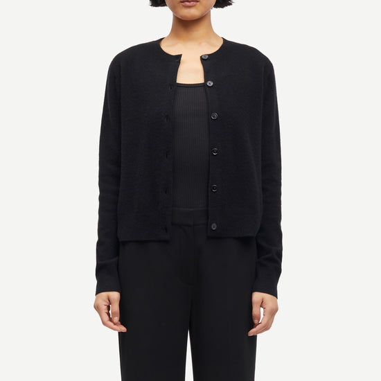 Person wearing a black cashmere cardigan over a black top and pants on a white background from Samsoe Samsoe
