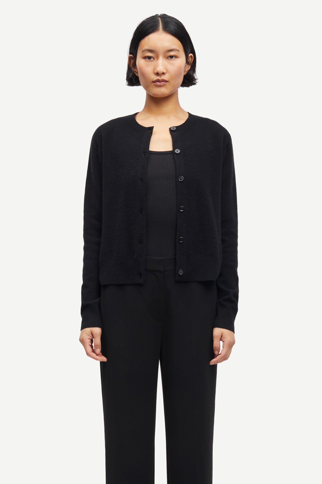 Person wearing a black cashmere cardigan over a black top and pants on a white background from Samsoe Samsoe