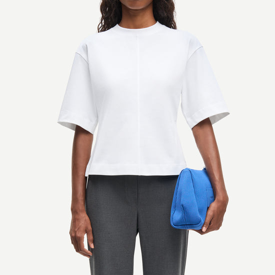 Woman wearing a white top and gray pants, holding a blue clutch against a white background from Samsoe Samsoe