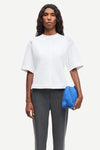 Woman wearing a white top and gray pants, holding a blue clutch against a white background from Samsoe Samsoe