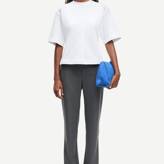 Woman wearing a white top and gray pants holding a blue clutch against a white background from Samsoe Samsoe