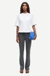 Woman wearing a white top and gray pants holding a blue clutch against a white background from Samsoe Samsoe