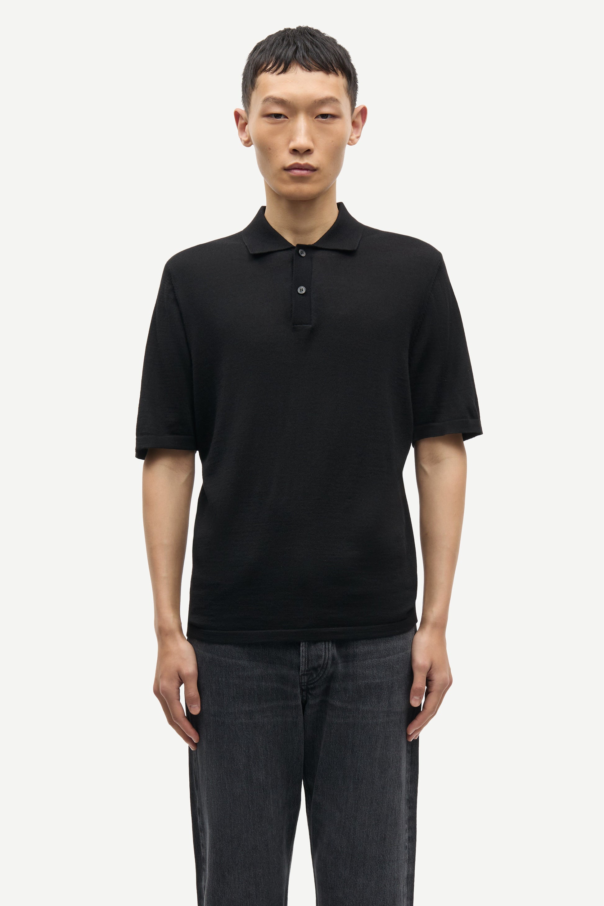 Man wearing a black polo shirt and dark jeans on a white background from Samsoe Samsoe