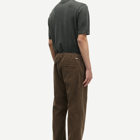 Person wearing a green polo shirt and brown pants on a white fbackground from Samsoe Samsoe