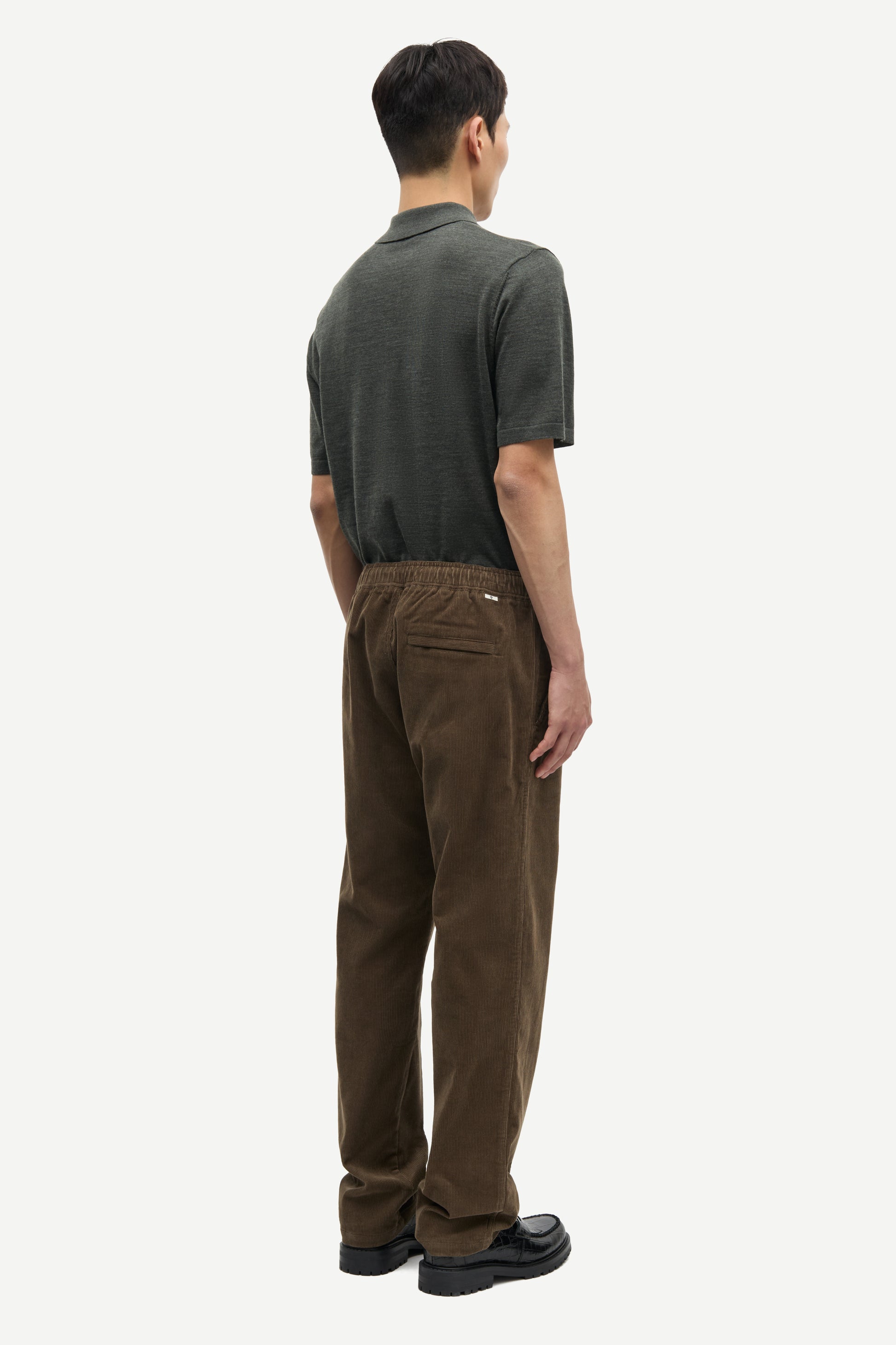 Person wearing a green polo shirt and brown pants on a white fbackground from Samsoe Samsoe