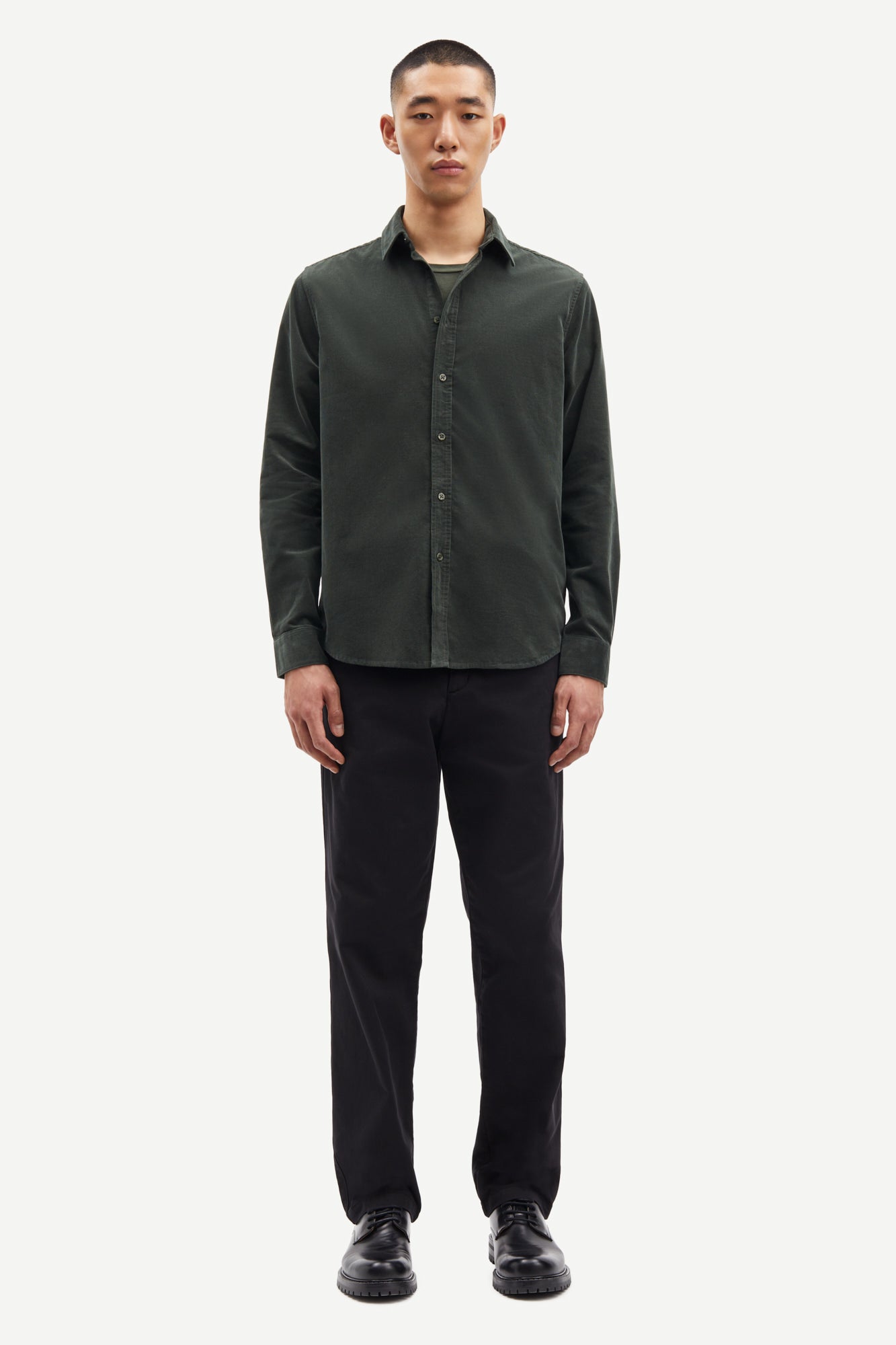 Man wearing a dark green button-up shirt and black pants on a white background from Samsoe Samsoe