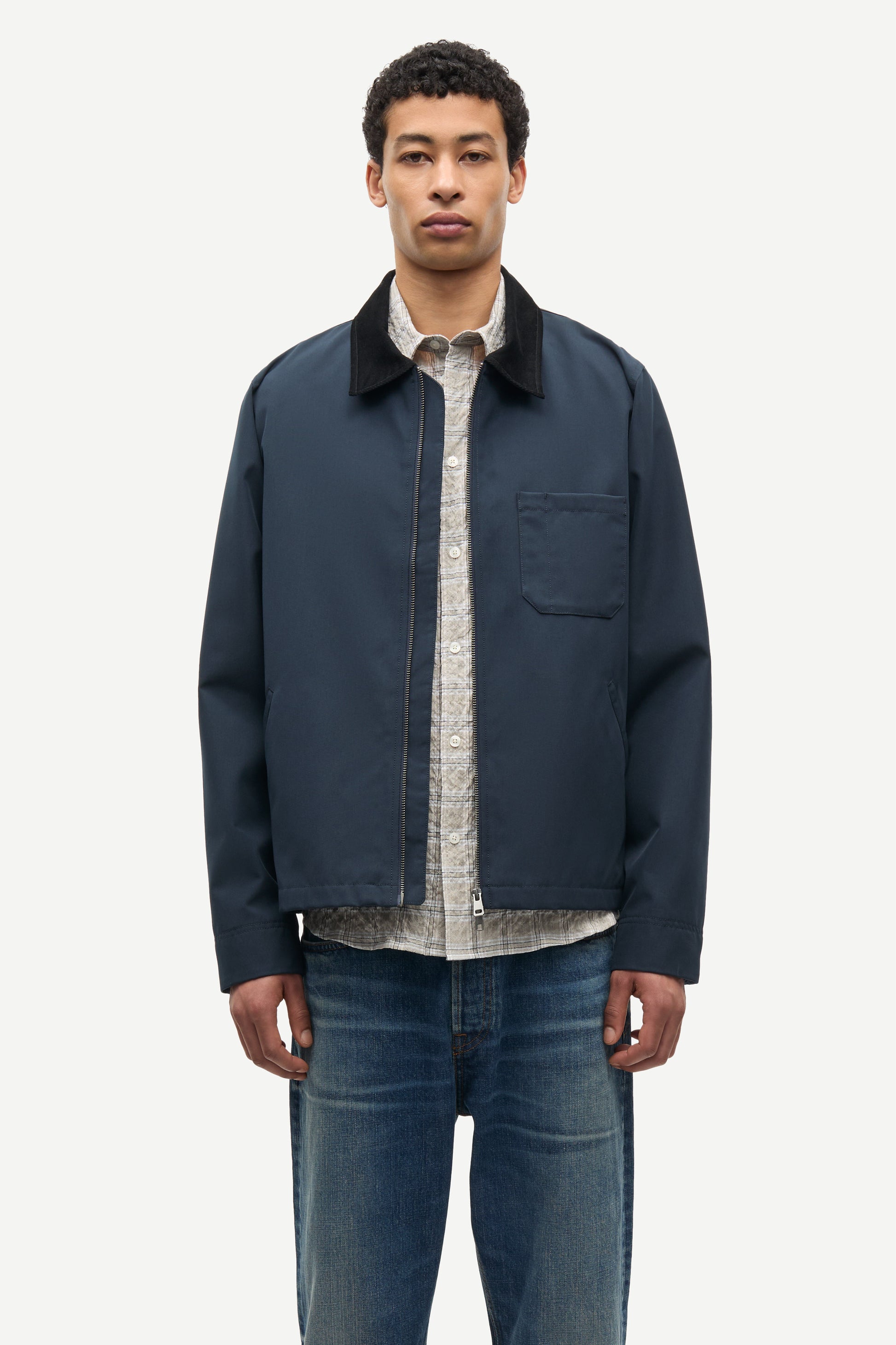 Man wearing a navy jacket over a patterned shirt with blue jeans on a white background from Samsoe Samsoe