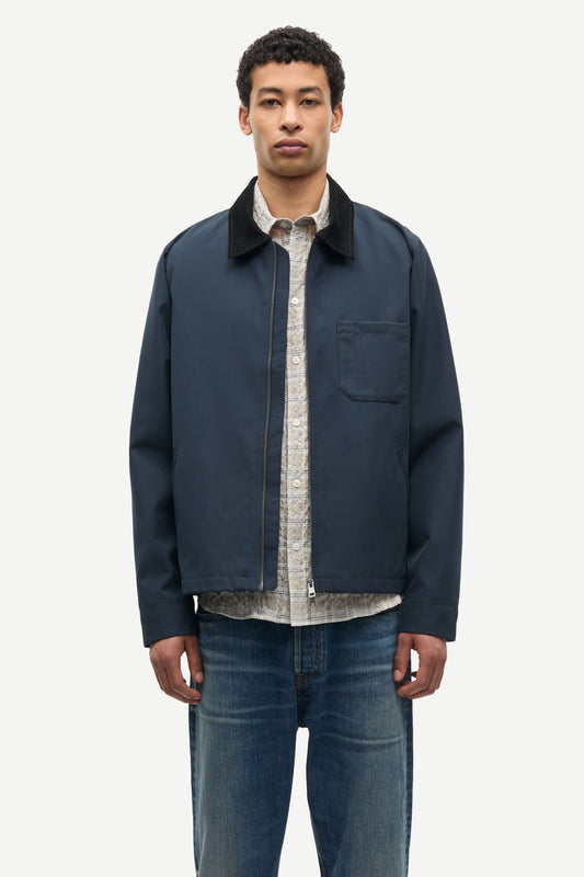 Man wearing a navy jacket over a patterned shirt with blue jeans on a white background from Samsoe Samsoe