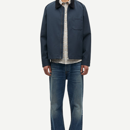 Man wearing a navy jacket, light shirt, and jeans on a white background from Samsoe Samsoe