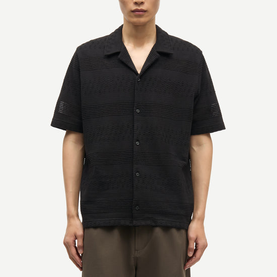 Man wearing a black textured shirt and brown shorts on a white background