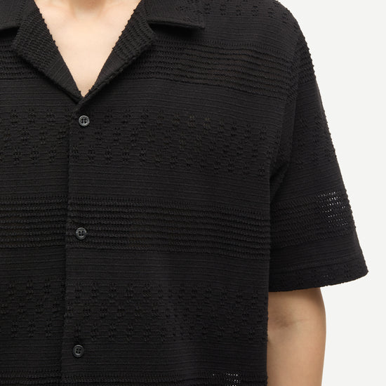 Black textured short-sleeve shirt worn by a person on a white background