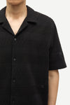 Black textured short-sleeve shirt worn by a person on a white background