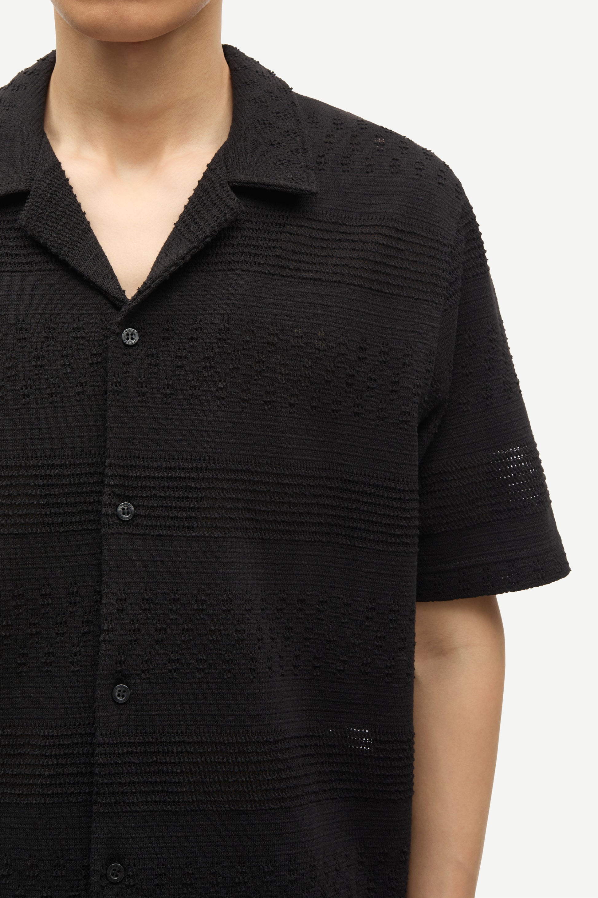 Black textured short-sleeve shirt worn by a person on a white background