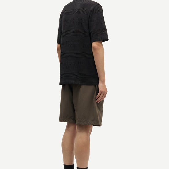 Person wearing a black polo shirt and brown shorts on a white background