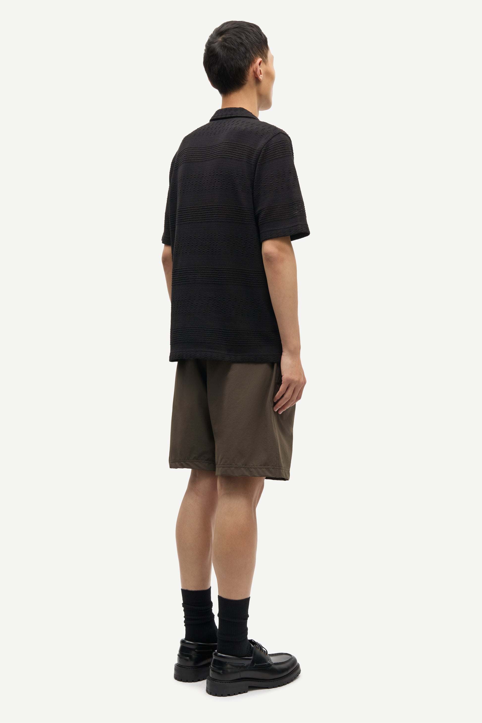 Person wearing a black polo shirt and brown shorts on a white background