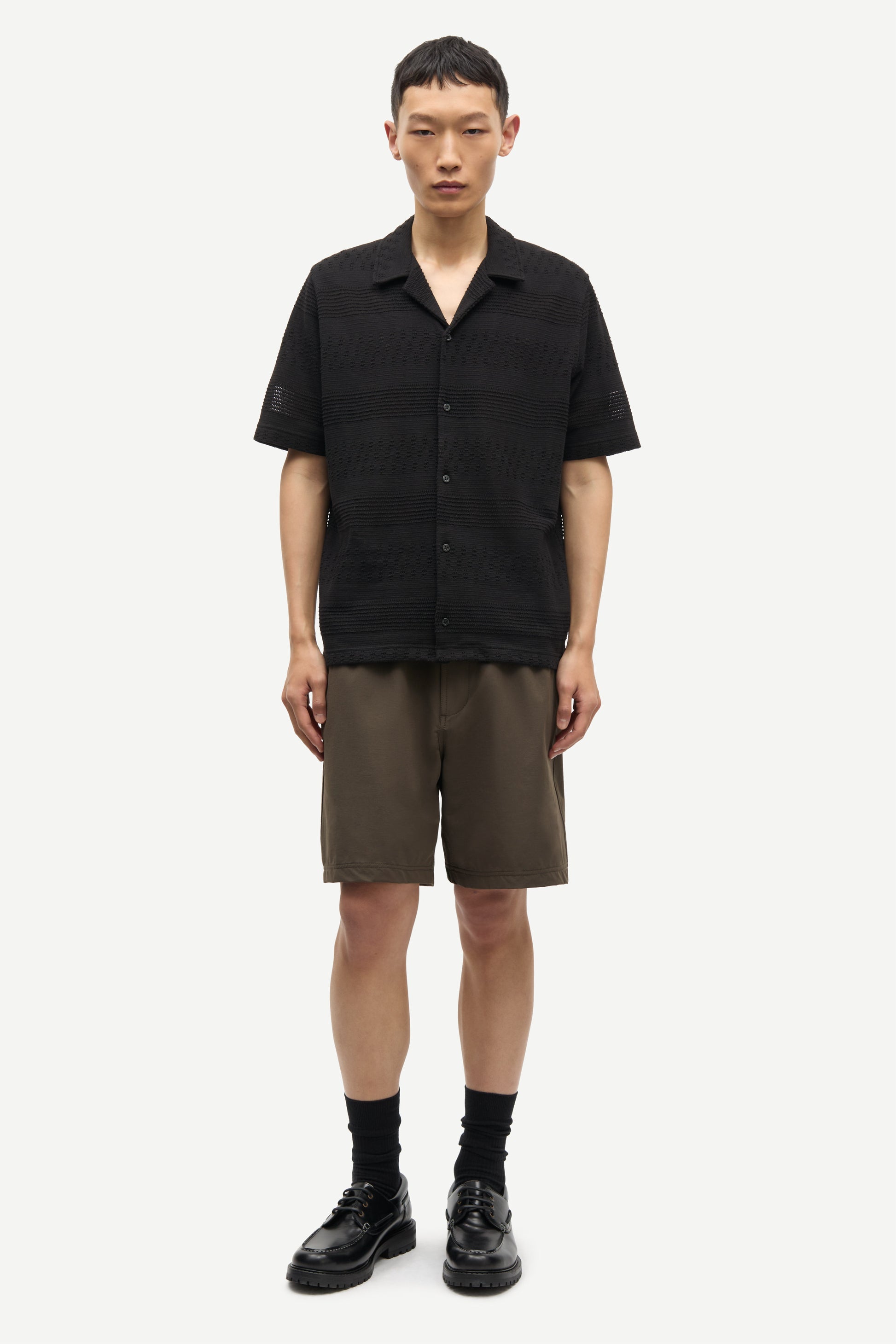 Man wearing a black short-sleeve shirt and brown shorts on a white background