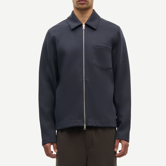 Man wearing a navy jacket with a zipper and a pocket on a white background