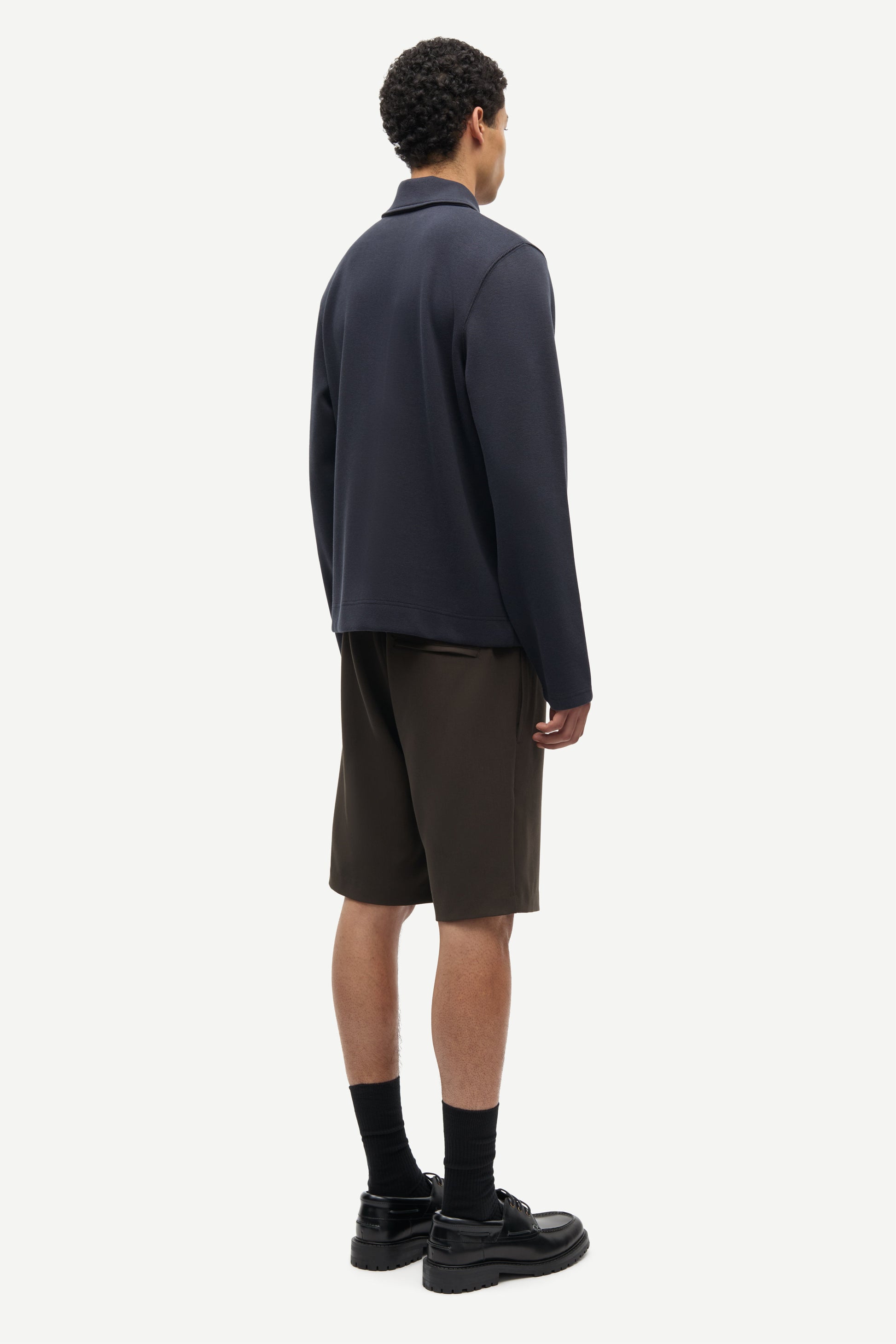 Person wearing a dark jacket and brown shorts on a white background