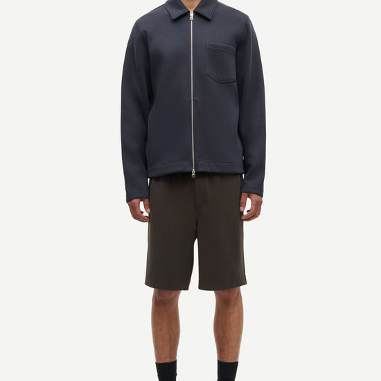 Person wearing a dark jacket and black shorts on a white background