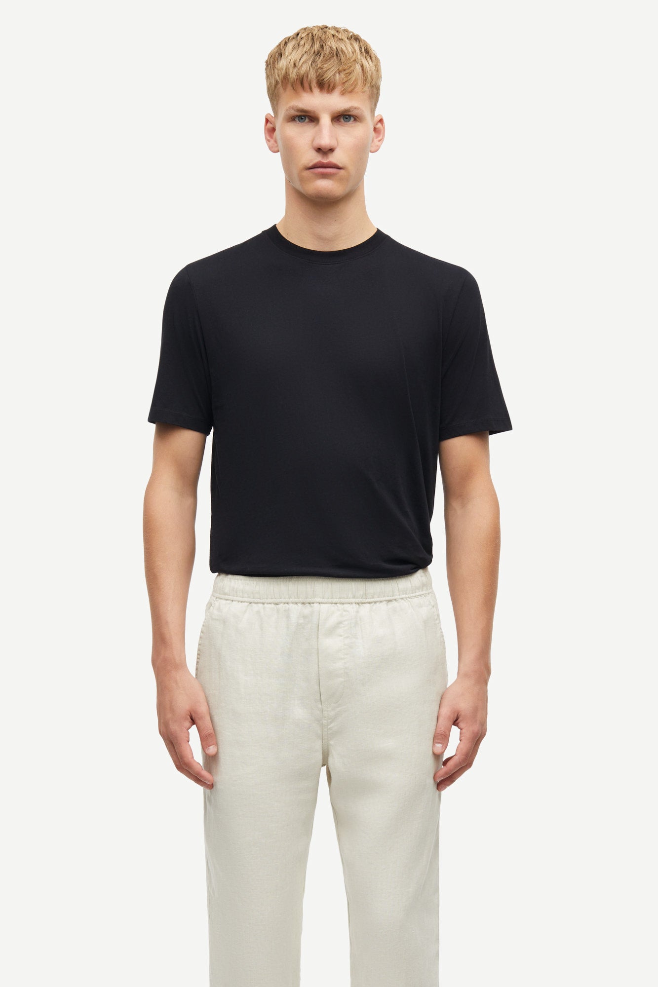 Man wearing a black t-shirt and white pants on a white background