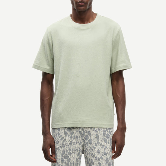 Man wearing a light green t-shirt and patterned shorts on a white background