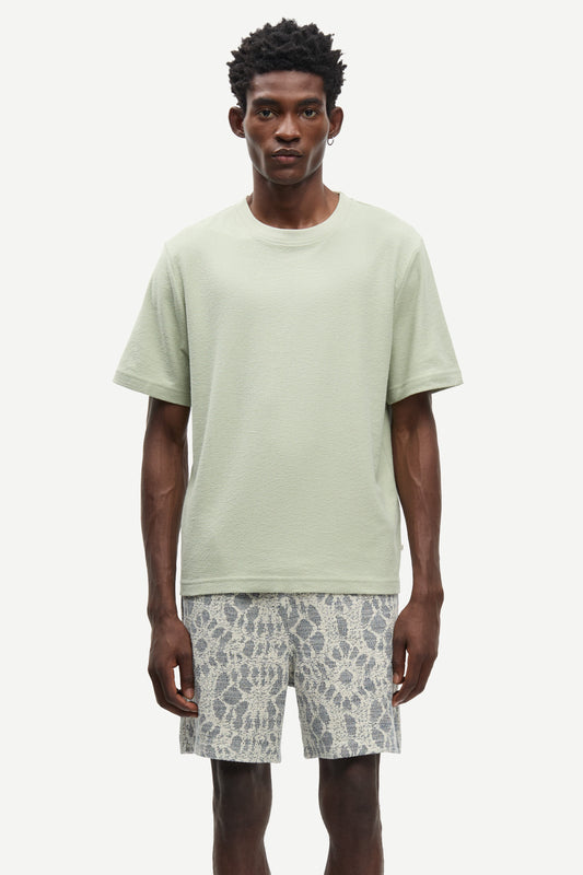 Man wearing a light green t-shirt and patterned shorts on a white background